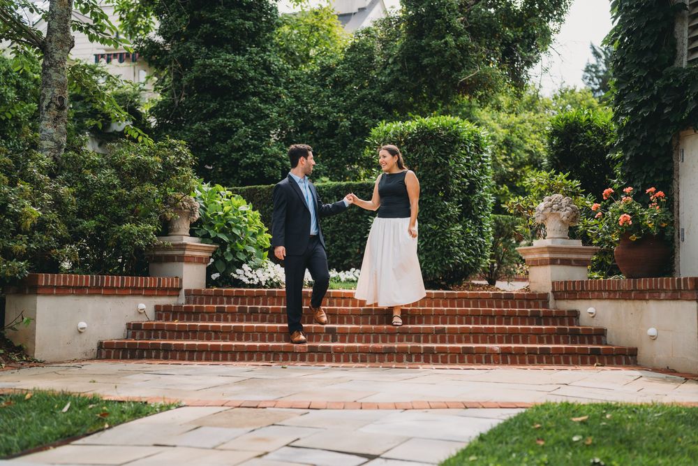 Couple holding hands on brick steps in a lush garden, man in blue blazer, woman in white skirt at inn at little washington