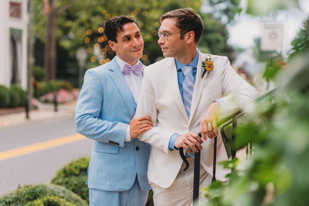 Two grooms in light blue and ivory suits smile at each other outdoors on their wedding day at inn at little washington