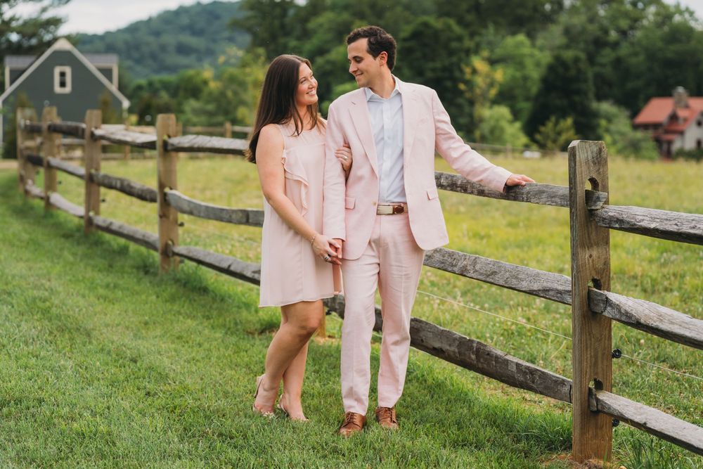 Couple in matching pink outfits holding hands by a rustic wooden fence in a green countryside setting at inn at little washington