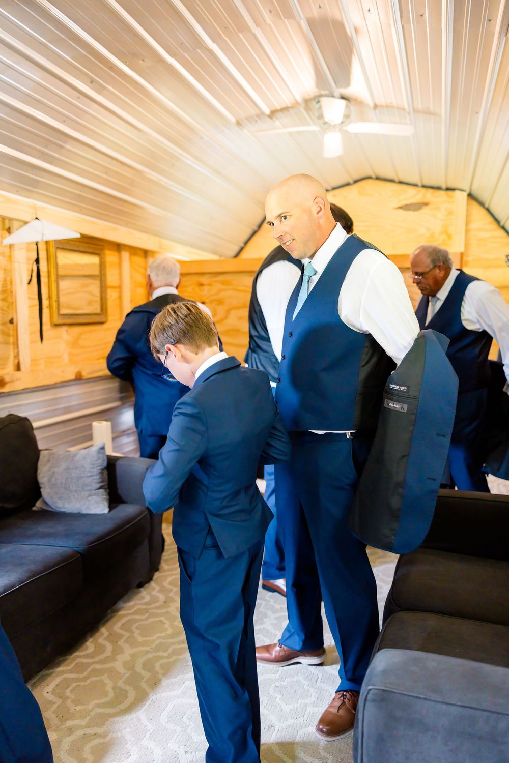 Groomsmen in navy blue suits preparing for a wedding ceremony in a rustic wood-paneled room.