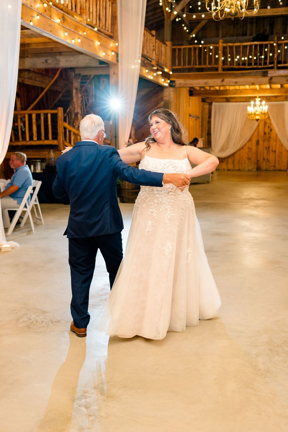 Bride and groom share a first dance in a rustic barn venue with warm string lights.