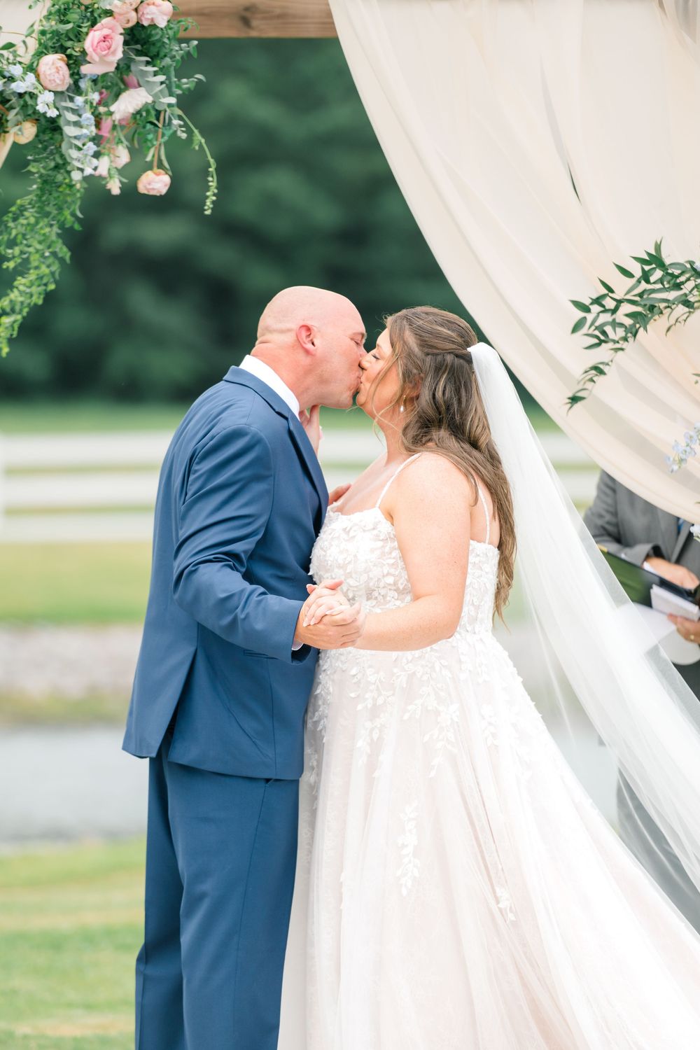 Bride and groom share their first kiss under a floral arch at an outdoor wedding ceremony.