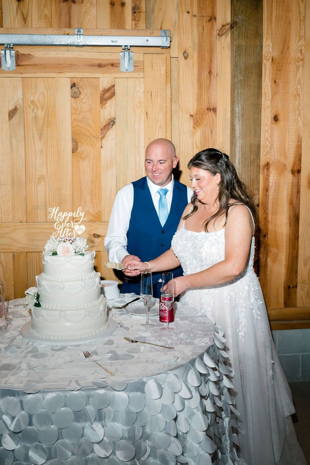 Bride and groom cutting their white tiered wedding cake at a rustic barn venue reception.