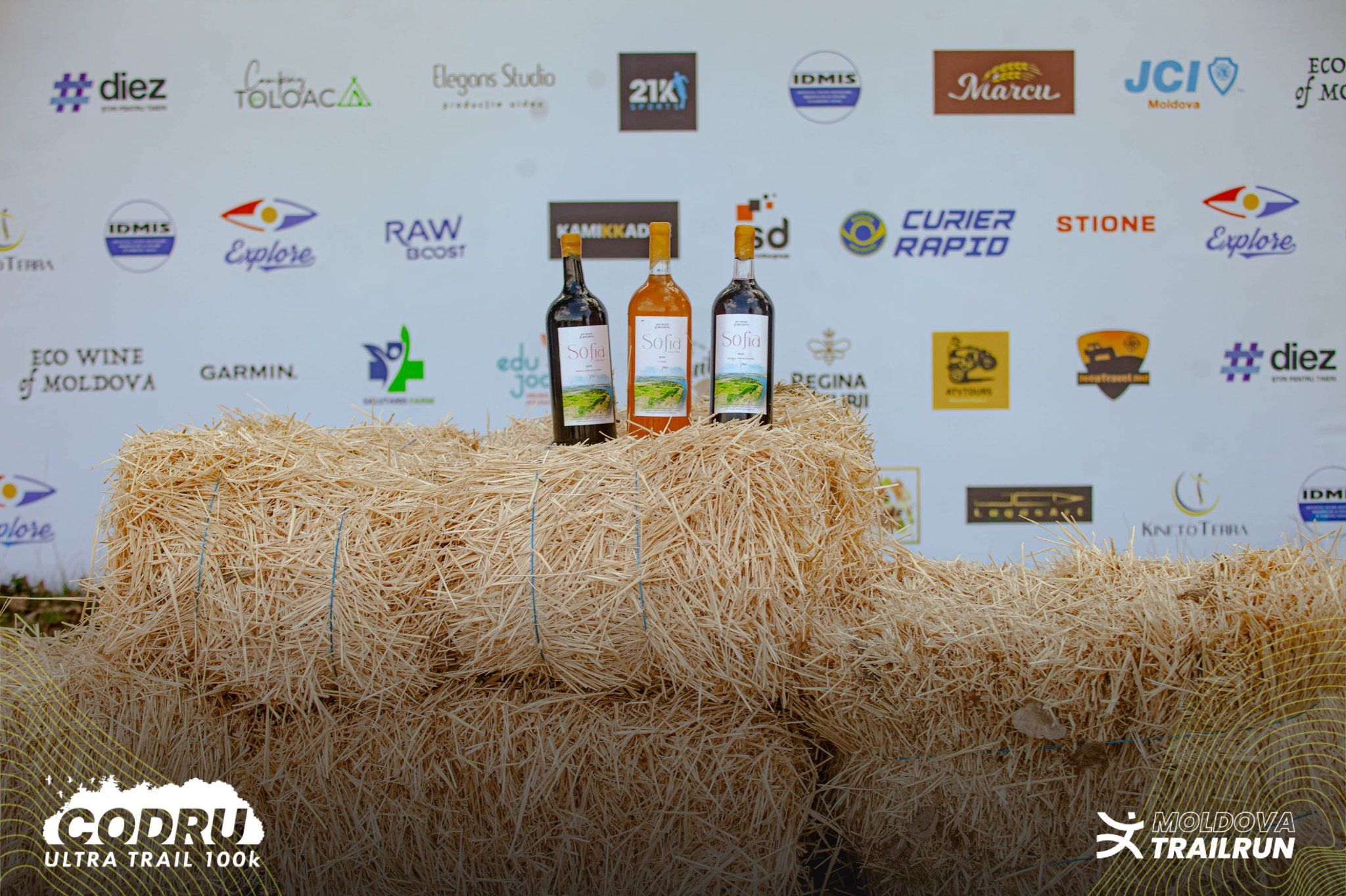 Three wine bottles displayed on hay bales at the Codru Ultra Trail 100k sponsored event backdrop.