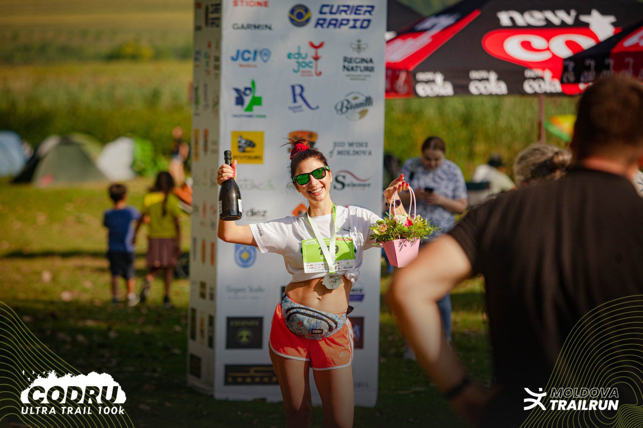 Female runner celebrating at the finish line of the Codru Ultra Trail 100k race holding a bottle.