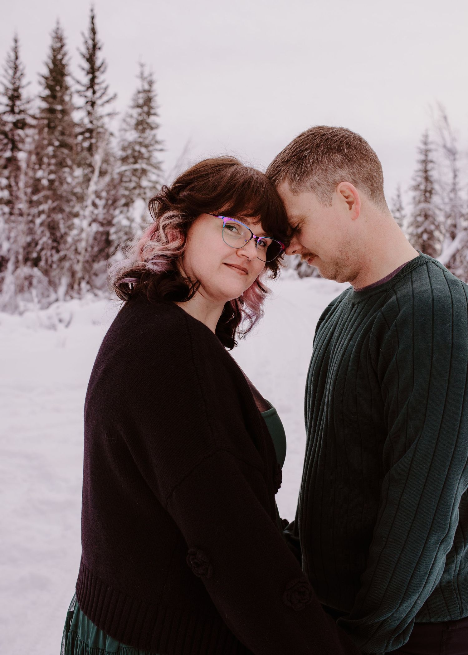 Couple standing together in a snowy winter forest during an outdoor portrait session