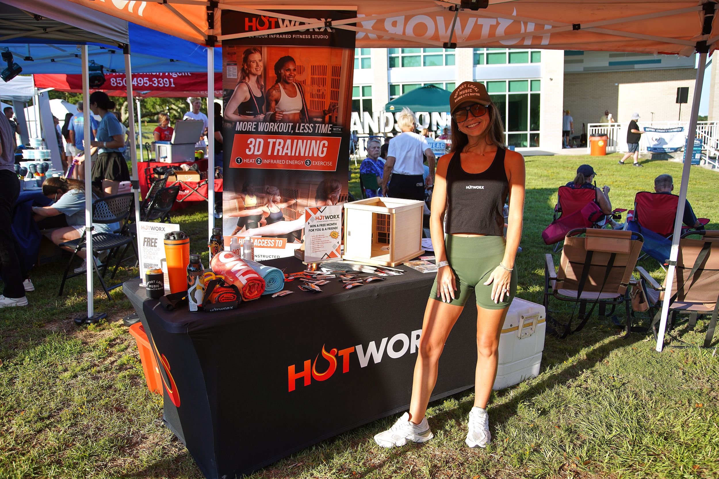 Woman standing at a HotWorx 3D training booth at an outdoor fitness expo event.
