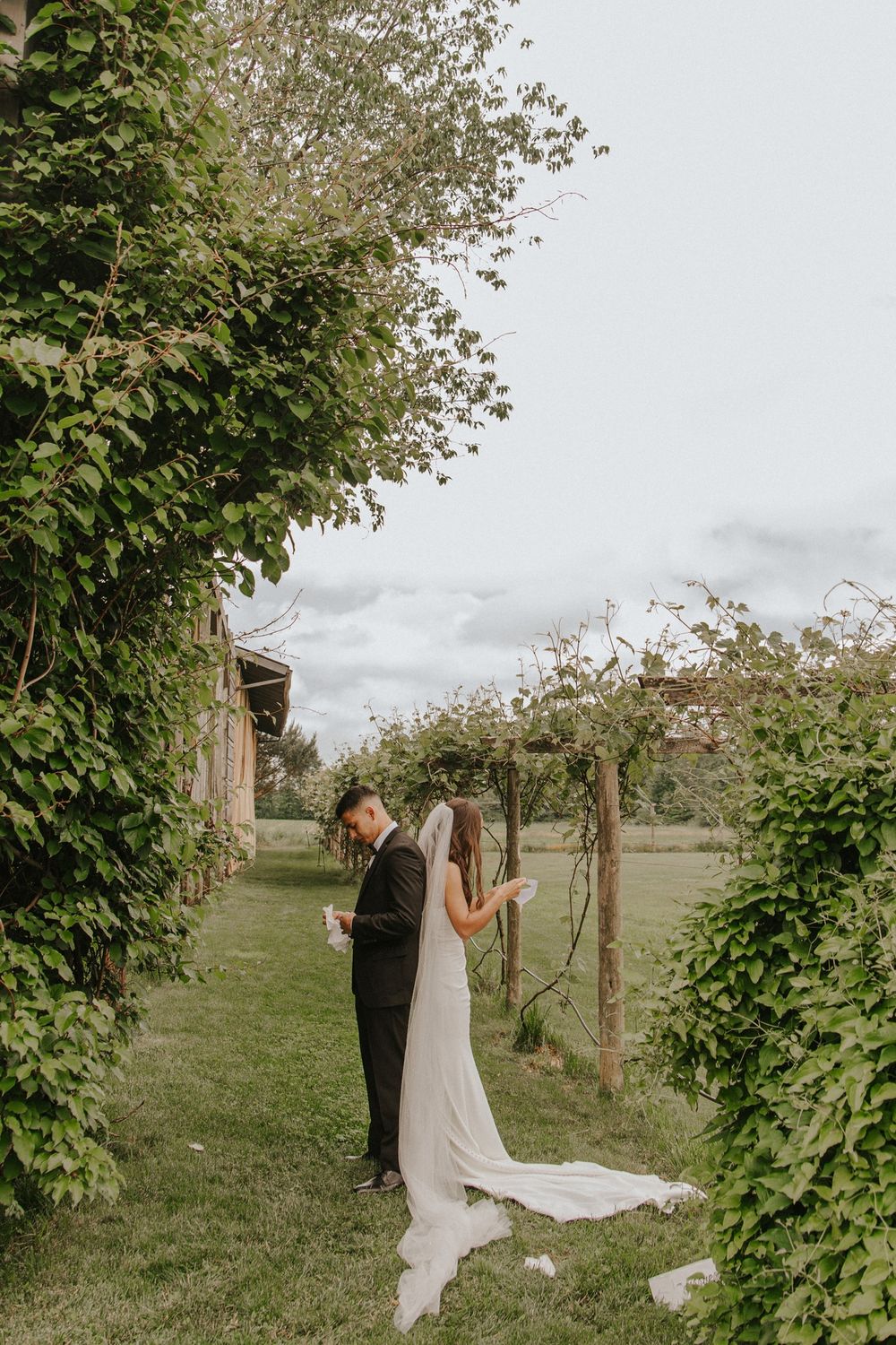 Bride and groom share a tender moment in a lush garden archway, bride in elegant white gown with veil.
