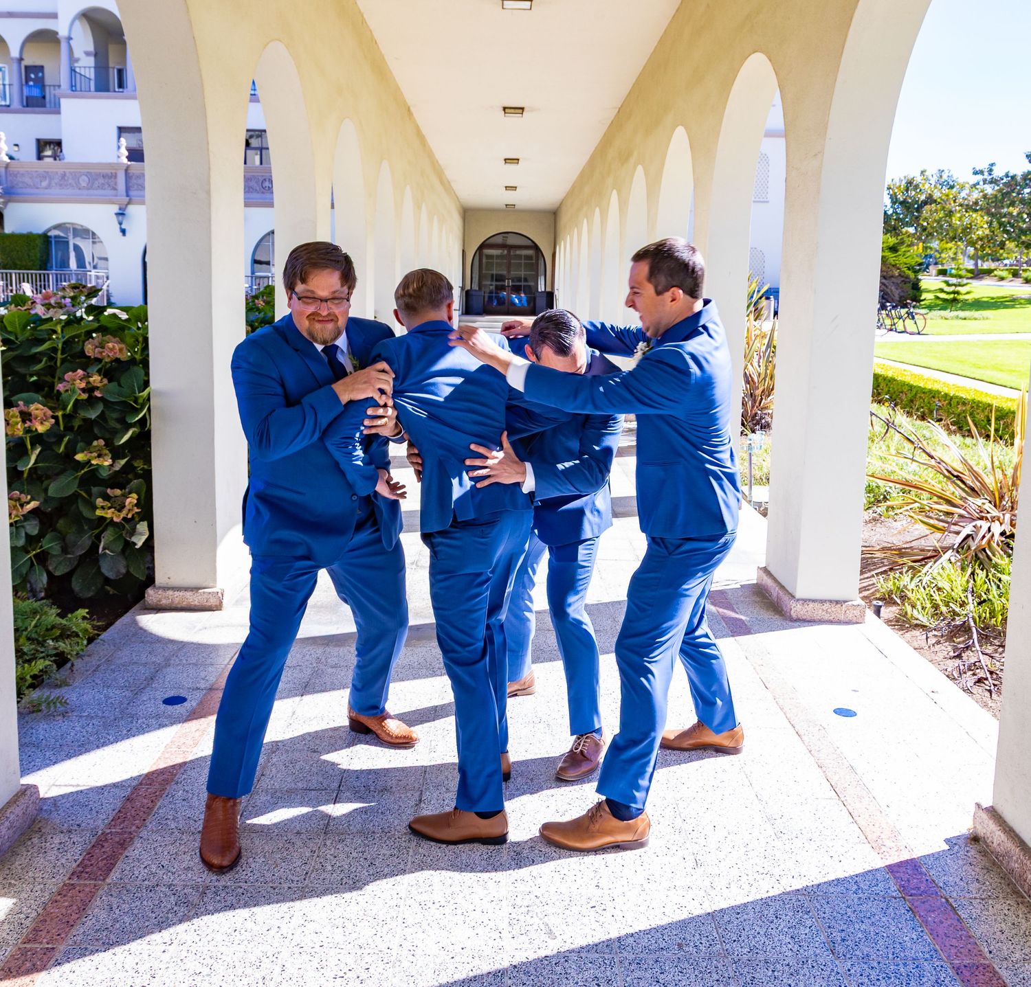 Groomsmen matching blue suits under a white columned archway. while being photographed. by Zeus Holbrook | San Diego Wedding Photographer