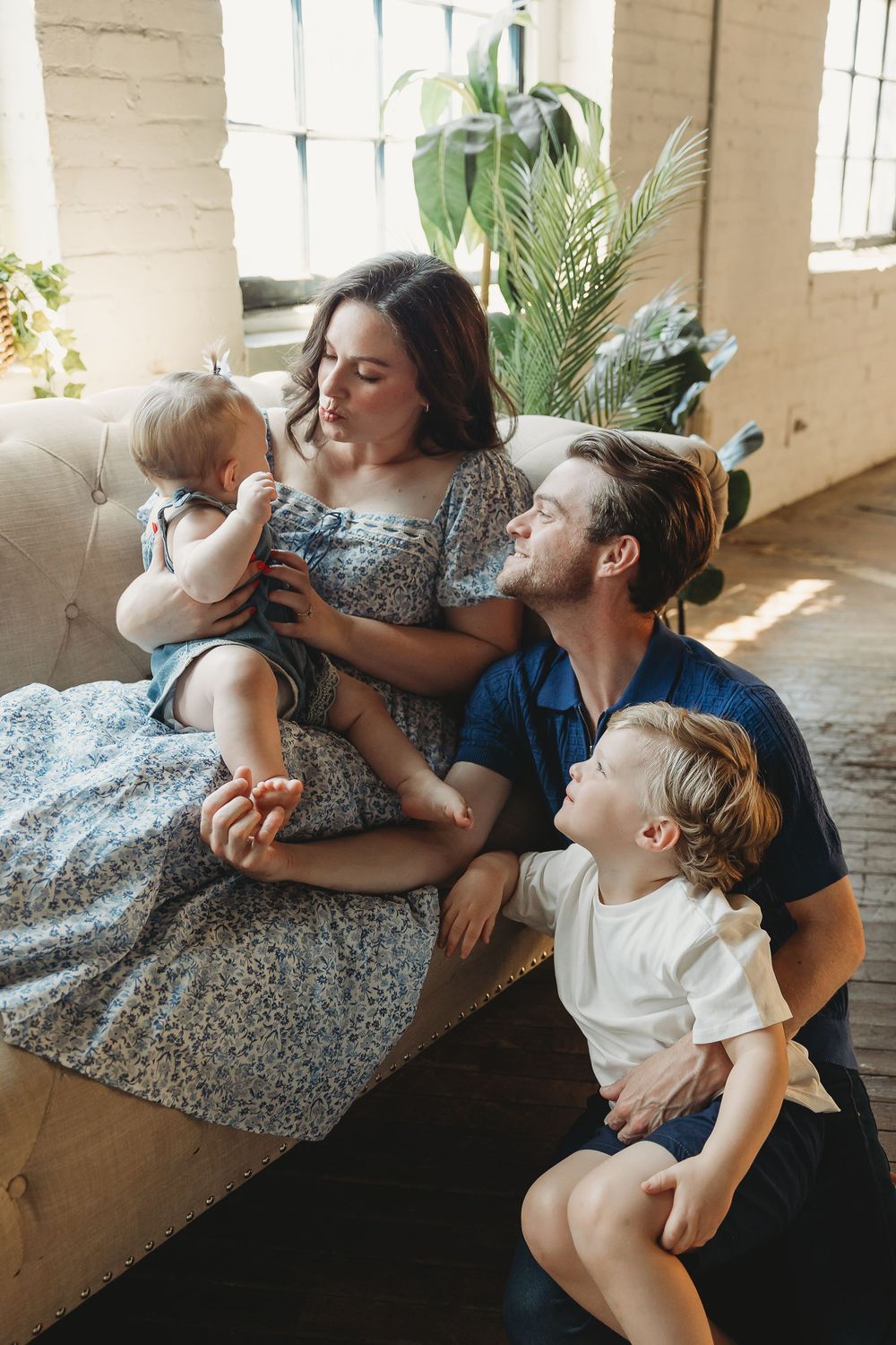 Happy young family with two toddlers relaxing together on a couch at home surrounded by indoor plants.