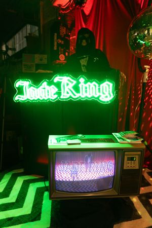 Jade Ring neon sign glowing green above a vintage CRT television in a dark, atmospheric bar setting.