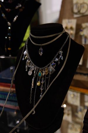Black velvet jewelry bust displaying layered necklaces with colorful gemstone charms and crystal pendants in a boutique setting.