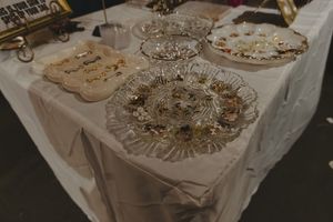 Crystal glass display plates arranged on white tablecloth showcasing gold and silver jewelry at a vendor market.