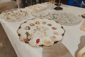 Vintage brooches and jewelry displayed on ornate crystal and white gold-rimmed plates on a white tablecloth.