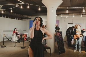 Woman in black dress talking on phone at an indoor art gallery event with string lights.