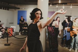 Woman in black dress poses gracefully at an indoor art market event.