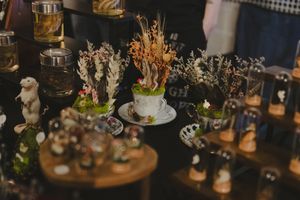 Whimsical miniature dried flower arrangements in teacups displayed on wooden stands at a craft market.