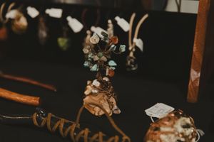 Handcrafted crystal and gemstone tree sculpture displayed on dark table among artisan goods at a market.