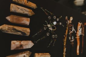Ornate spider jewelry piece surrounded by crystal points and wooden sticks on dark background.