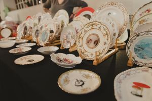 Collection of vintage decorative porcelain plates with artistic designs displayed on gold easels on black table.
