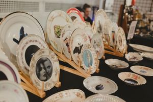 Vintage decorative plates displayed on wooden stands at a market, featuring portraits and artistic designs.