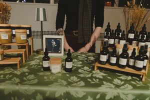 Vendor table displaying herbal tinctures and botanical skincare products on green floral cloth.