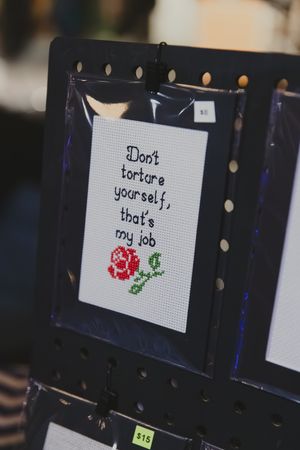 Cross-stitch artwork reading Don't torture yourself that's my job with red rose design.