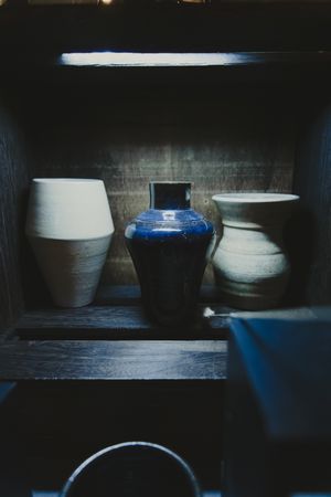 Three ceramic vases on a dark wooden shelf, including a blue glazed centerpiece.