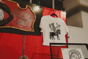 White graphic t-shirt with black horse print hanging in a red-decorated art studio.
