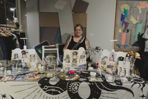 Woman vendor smiling behind a table of celestial-themed art prints and crystals at an indoor market.