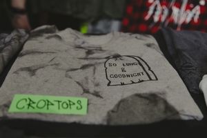 Gray crop top t-shirt with tombstone graphic reading So Long and Goodnight folded at vendor market booth.