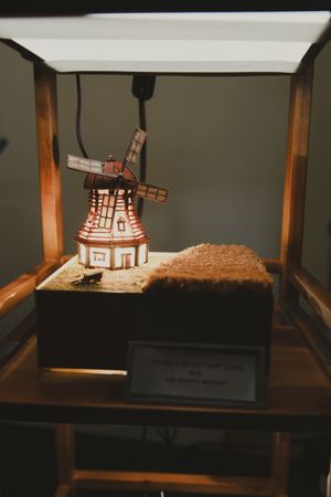 Miniature windmill model displayed in a wooden box under a light.