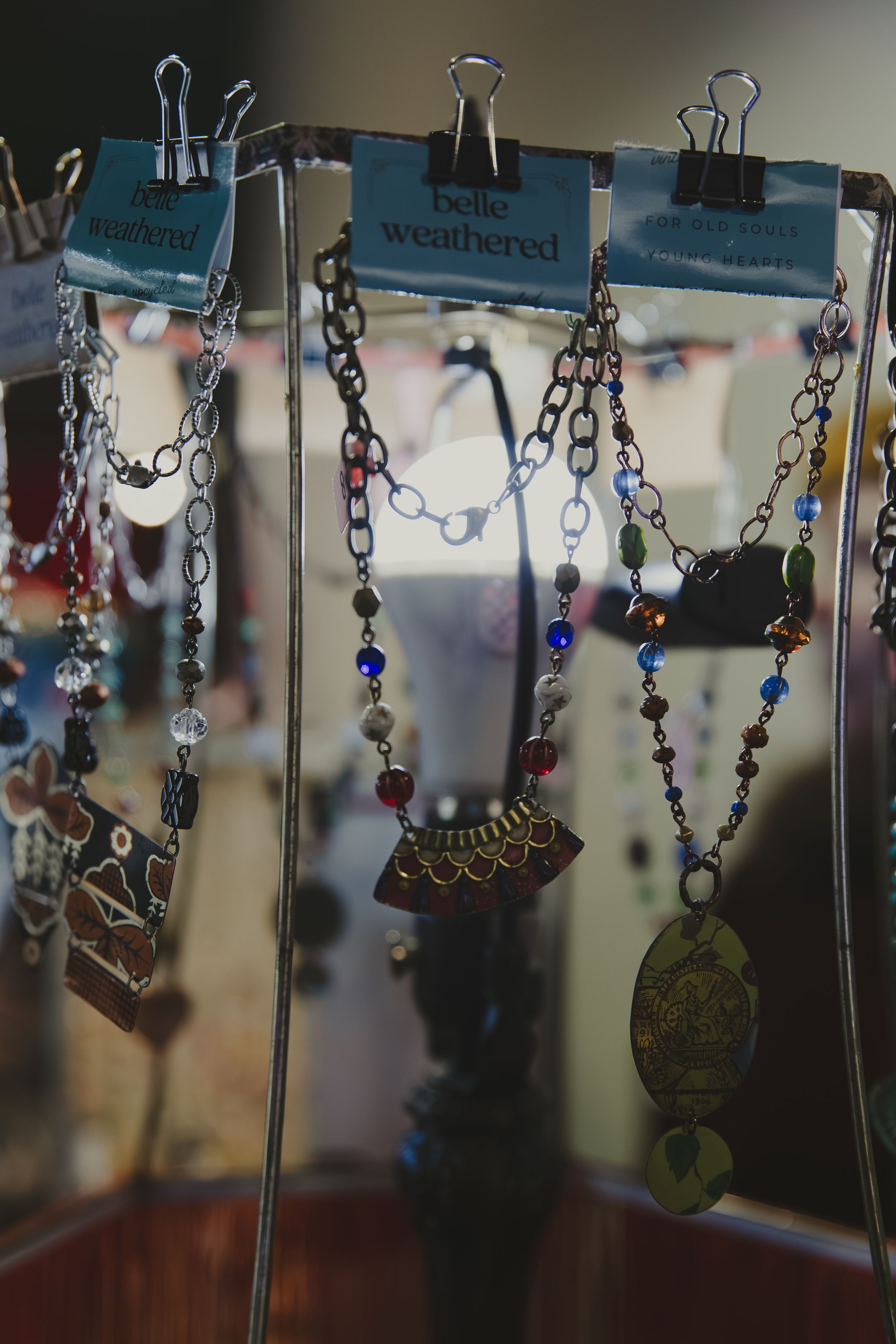Handmade beaded necklaces displayed on a rack with Belle Weathered tags at a jewelry boutique.