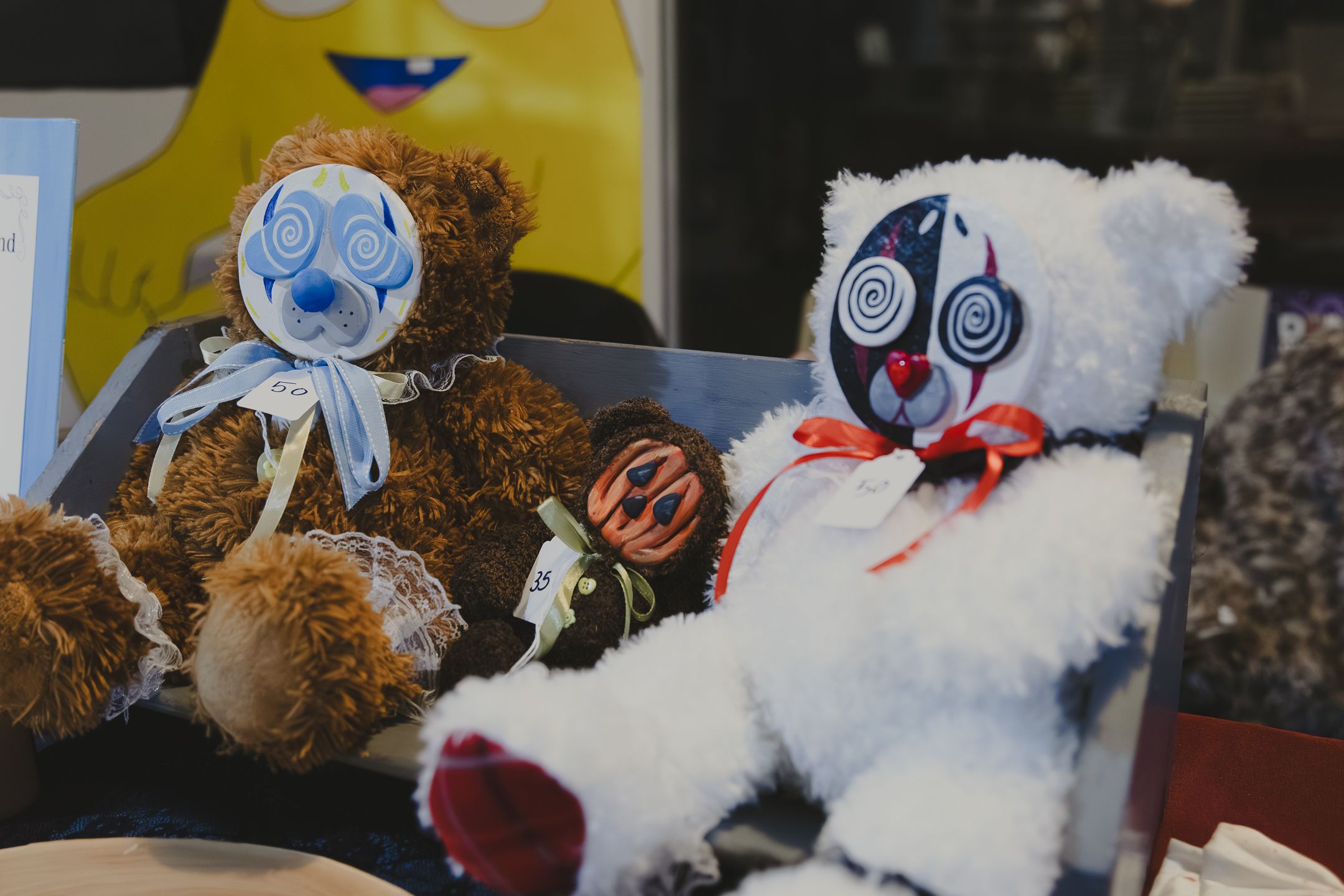 Two creepy teddy bears with swirling hypnotic eyes displayed in a box, one brown and one white with clown face paint.