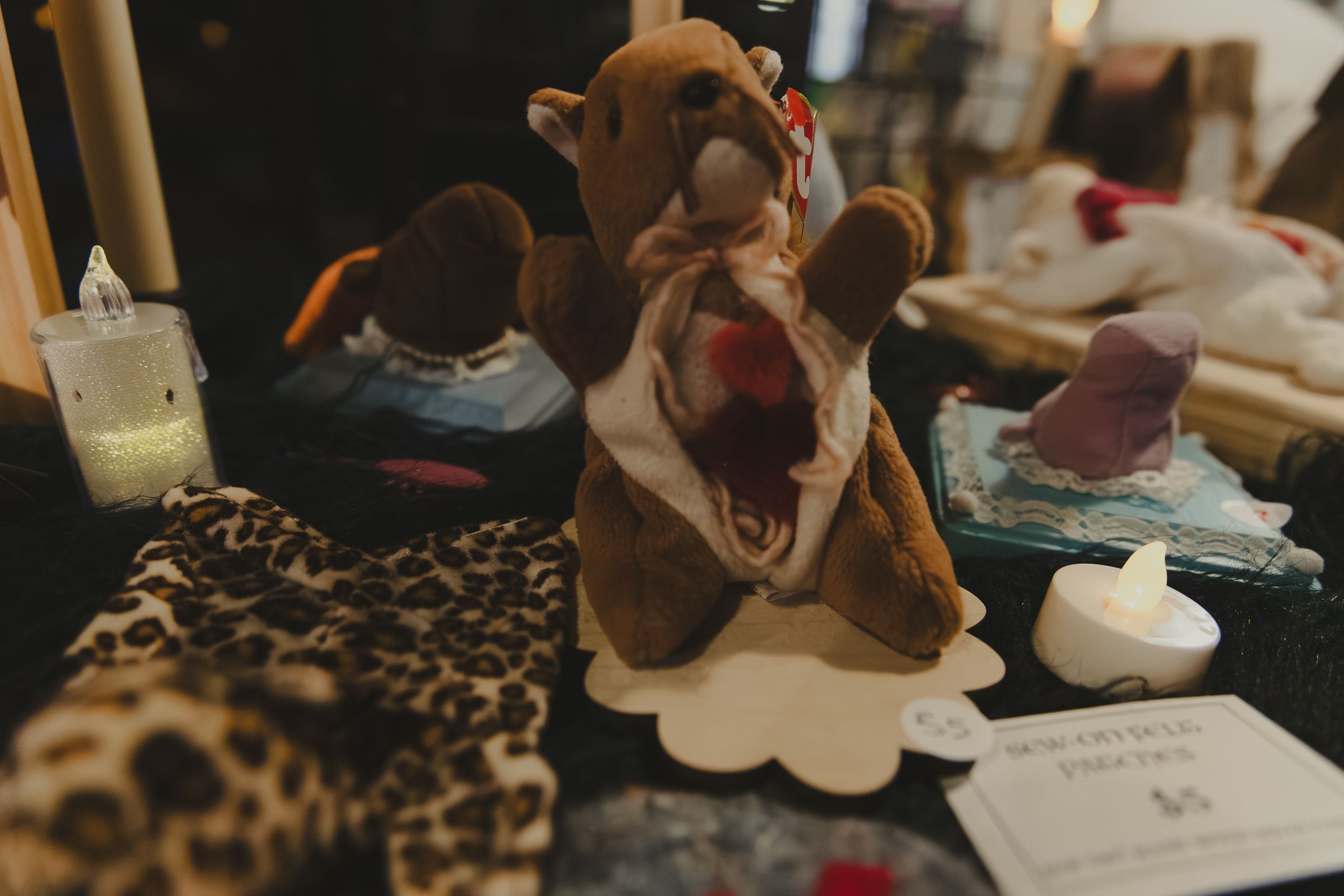 Brown bear hand puppet displayed on a table with leopard print fabric and candles at a craft market.
