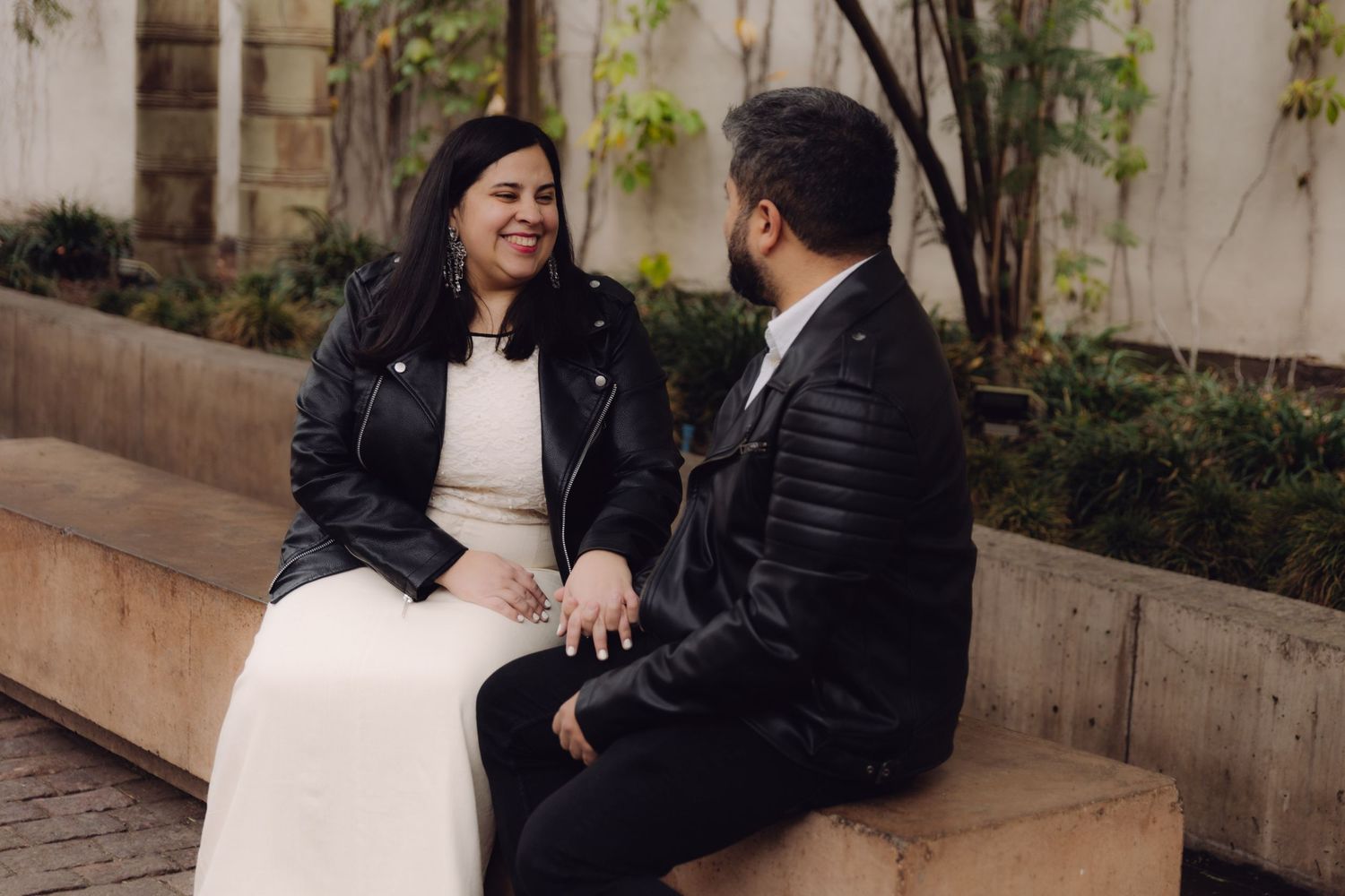 Couple in matching black leather jackets sitting on a stone bench, sharing an intimate conversation outdoors.
