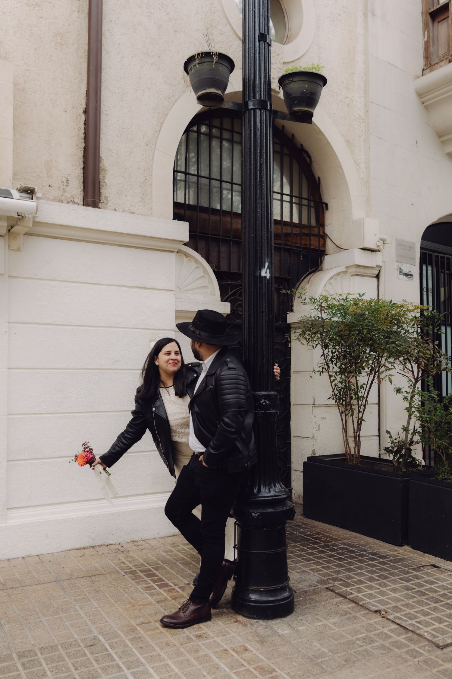 Stylish couple in black leather jackets standing by a vintage street lamp outside a historic building.