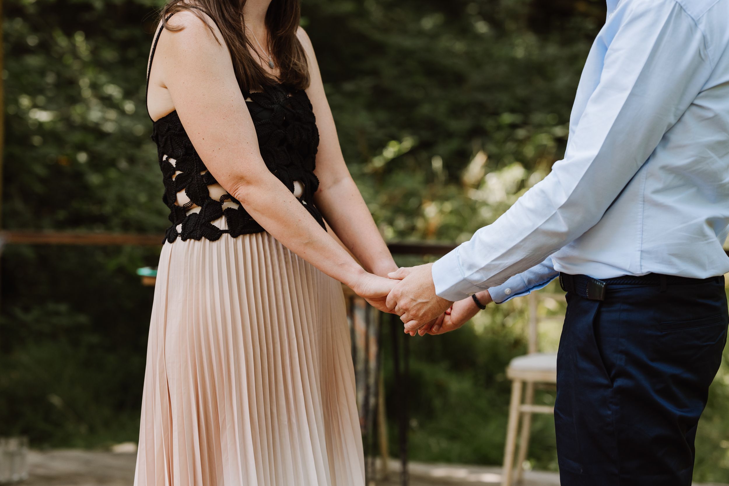 Couple holding hands outdoors at Moonacre, woman wearing pleated blush skirt and black lace top at romantic event.