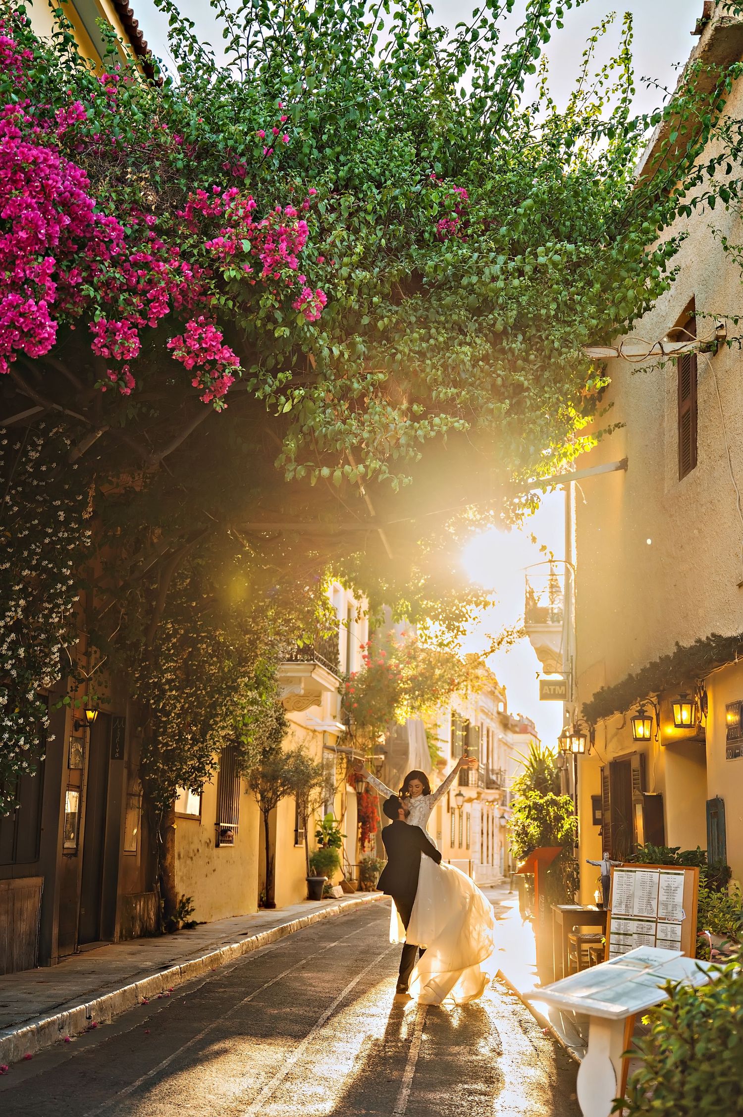 Couple dancing in a sunlit Mediterranean alley with bougainvillea blooms and golden hour light.
