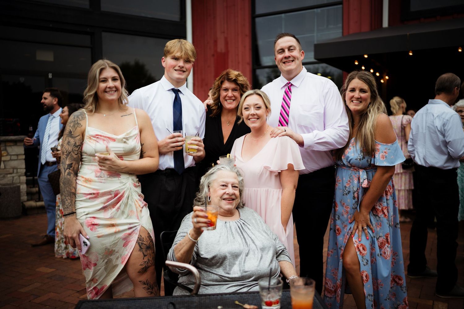A joyful family group poses together at an elegant outdoor wedding reception, dressed in formal attire.
