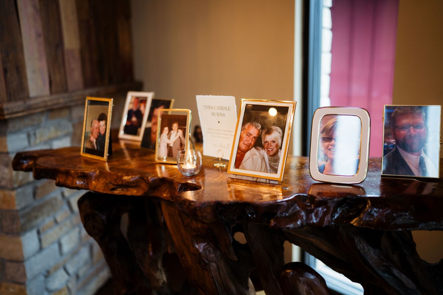 Framed family photos displayed on a rustic wooden table at a wedding venue with stone wall backdrop.