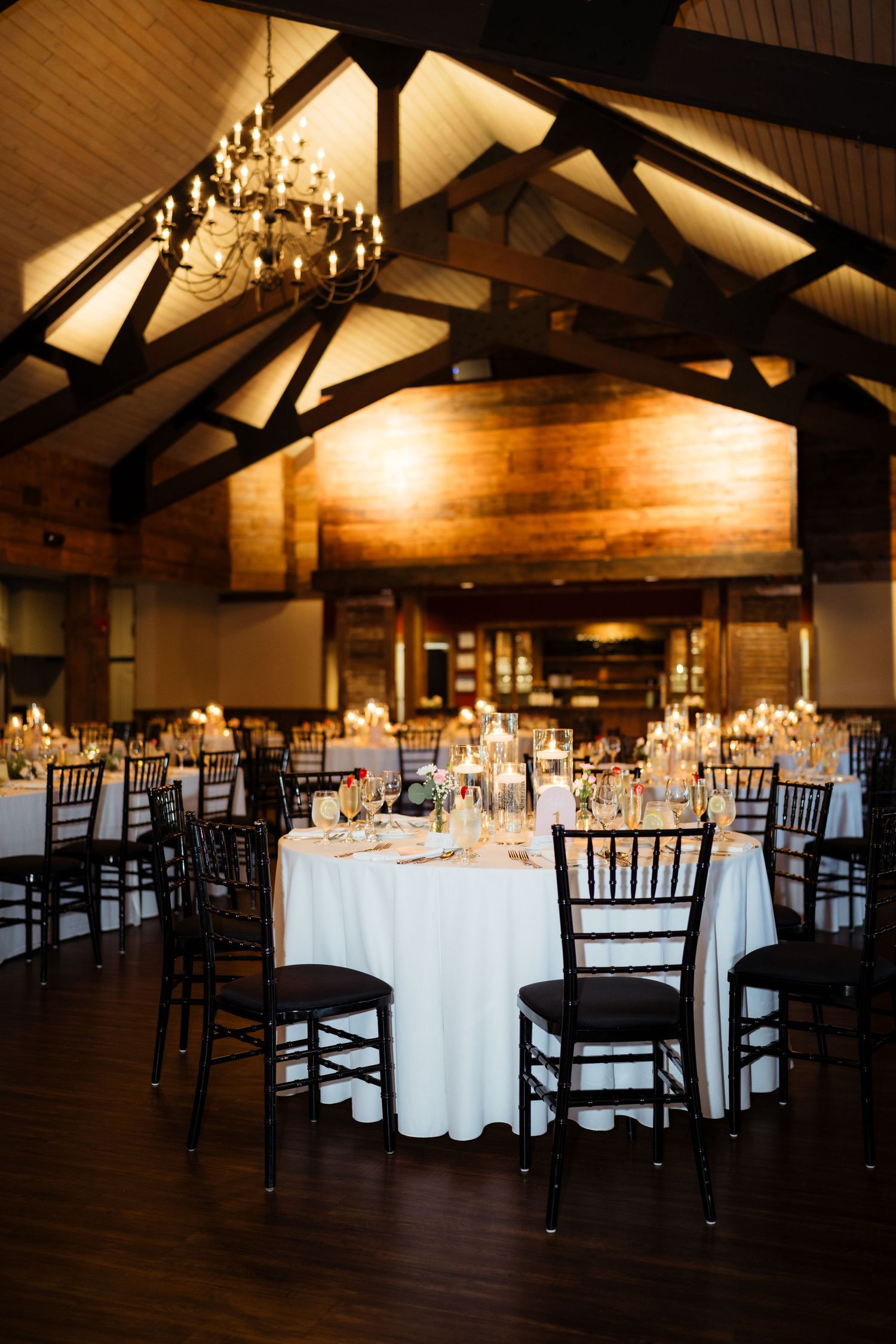 Elegant barn wedding reception hall with dark wood beams, chandelier, and round tables with white linens.