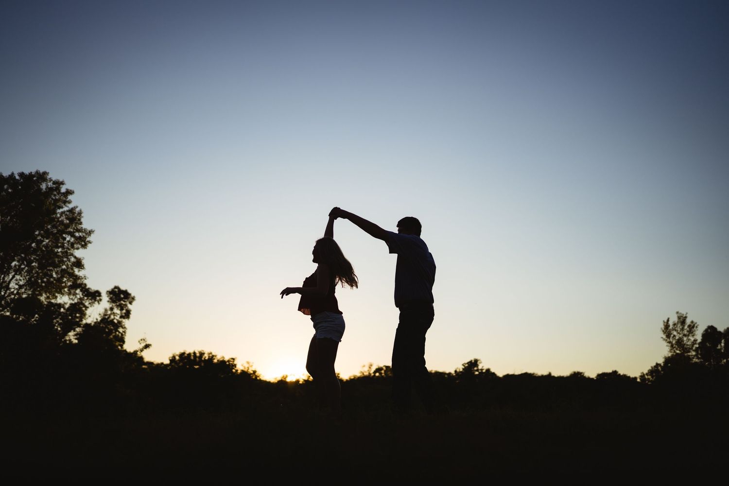 Silhouette of a couple dancing at sunset with trees in the background.