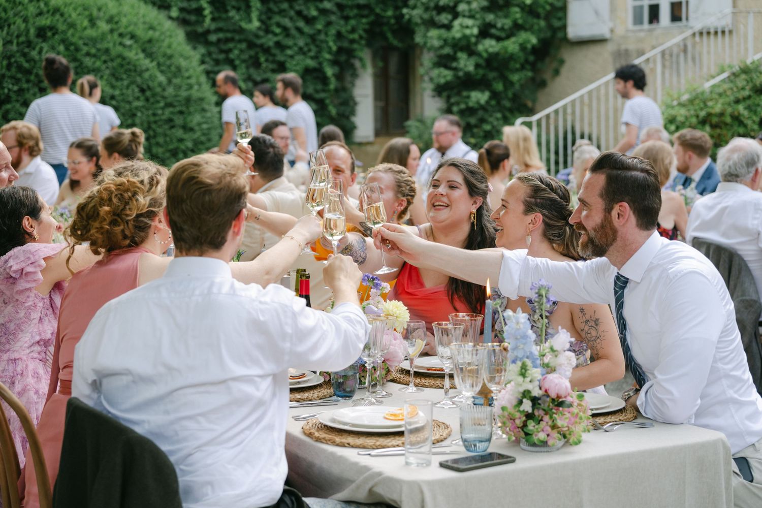 Guests raising glasses in a toast at an elegant outdoor wedding reception with floral centerpieces.