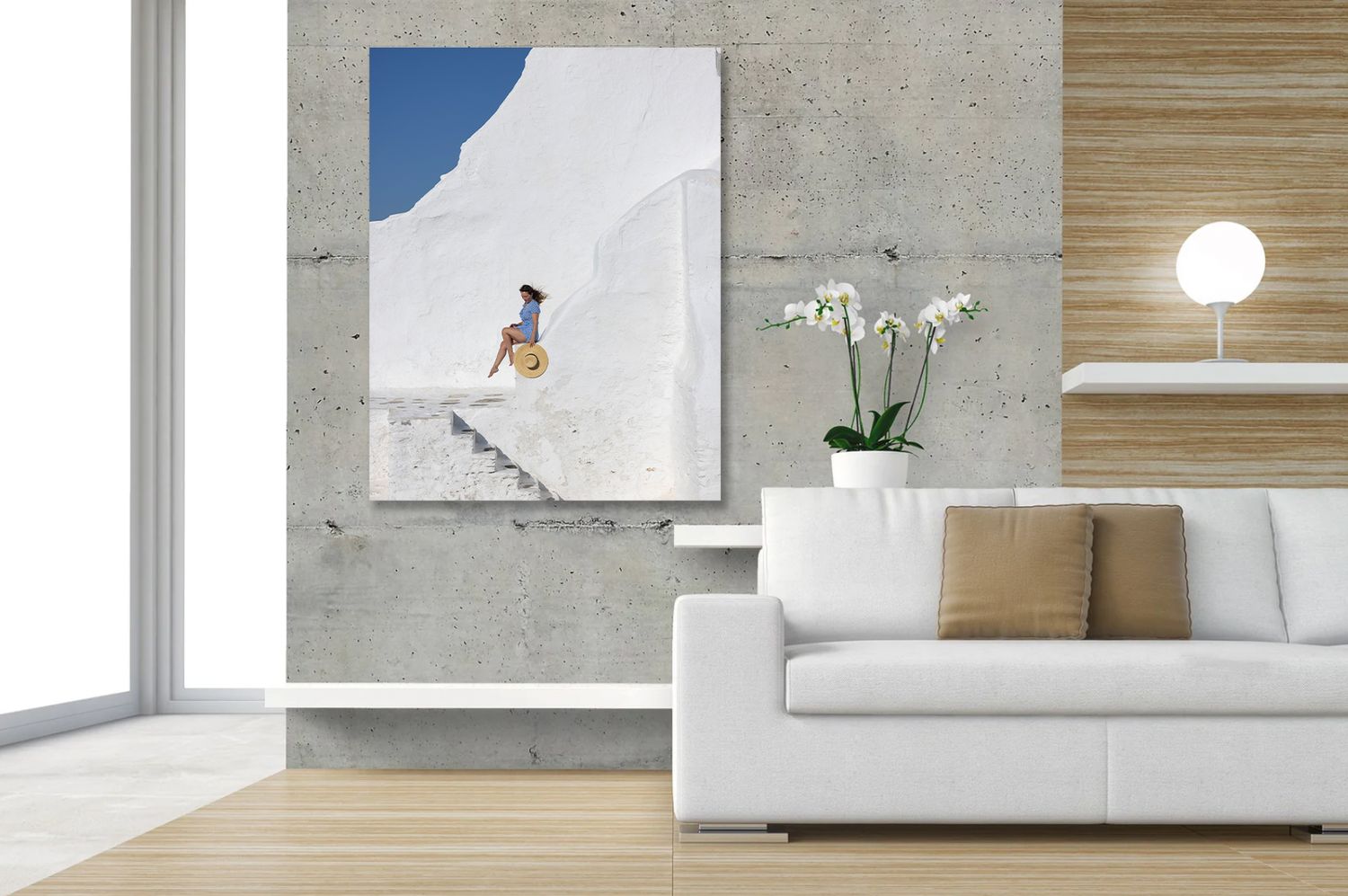 A large canvas print of a woman on white Santorini steps hangs in a modern living room with a white sofa.