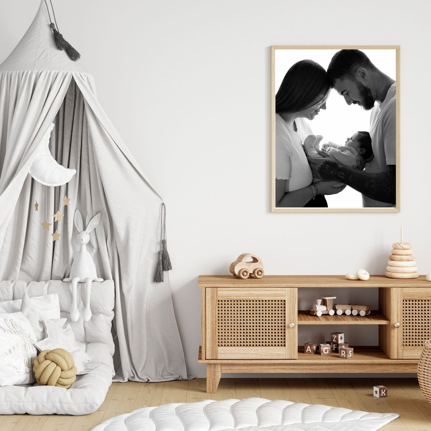 Black and white family portrait in wooden frame displayed in a cozy Scandinavian-style nursery with canopy bed and rattan dresser.