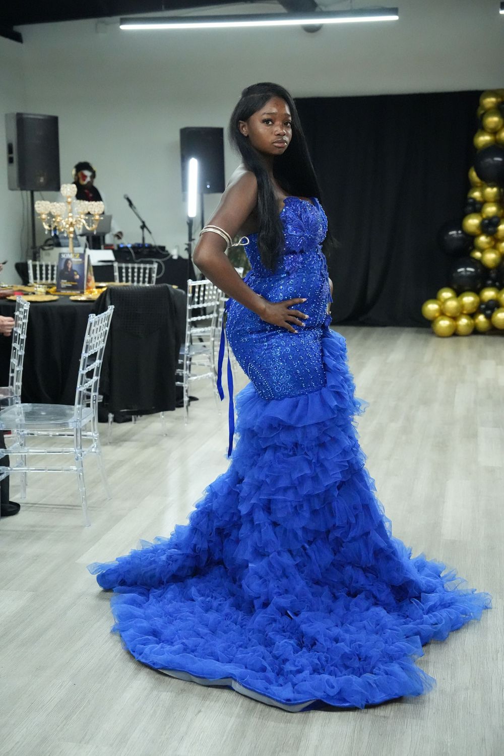 Model in royal blue sequined mermaid gown with ruffled train at fashion show event.