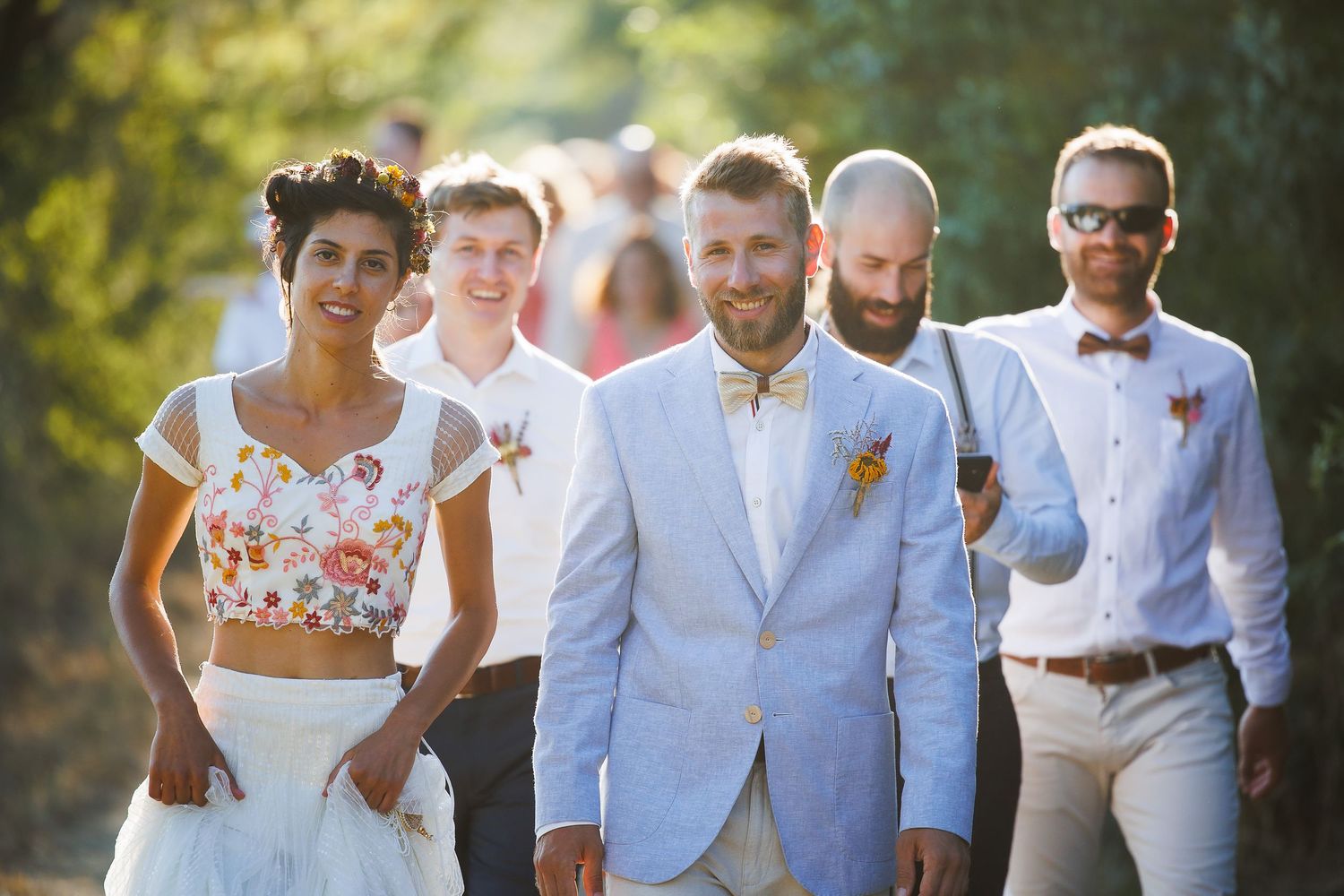 A bride and groom share an intimate moment, smiling together, as she holds a bouquet of red and white flowers.