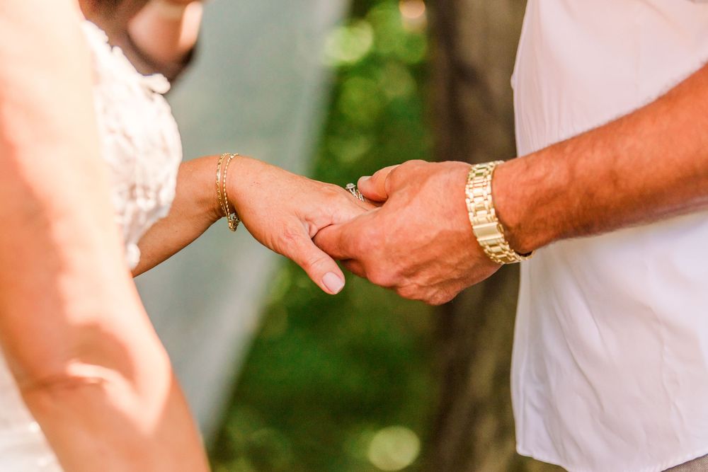 Close-up of a couple holding hands during a wedding ceremony, with a gold bracelet visible on the groom's wrist.