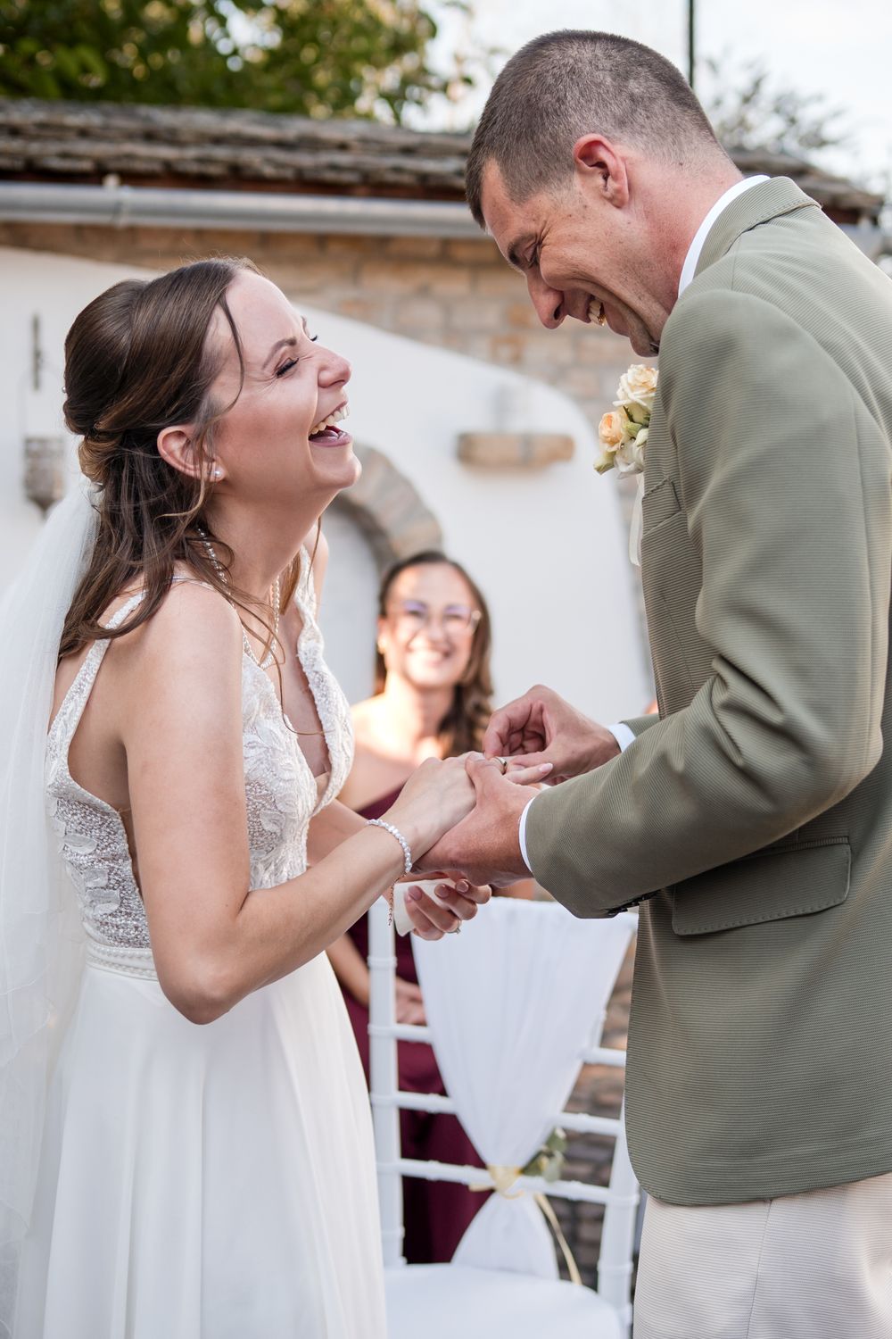Bride and groom laughing joyfully during ring exchange at outdoor wedding ceremony.